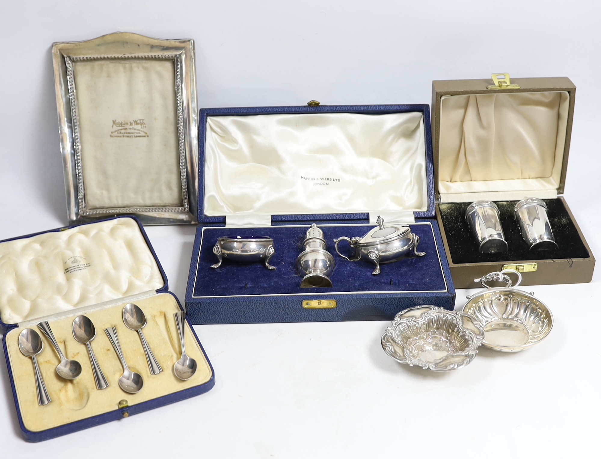 An Elizabeth II cased silver three piece condiment set by Mappin & Webb, a cased pair of Irish silver pepperettes, a cased set of six silver coffee spoons, two silver dishes and a silver mounted photograph frame.